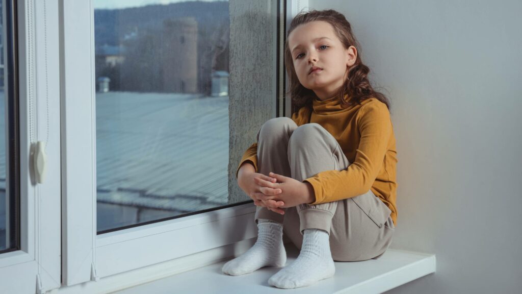 Autism. Little Girl on Window Sill Indoors